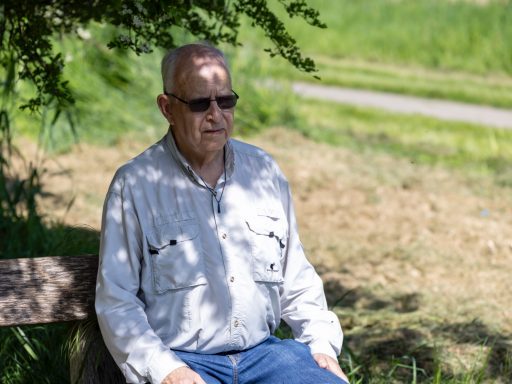 Oude man in een zonnebril zit op een bankje in de natuur.