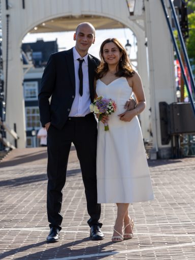Bruid en bruidegom poseren samen voor een brug, met een boeket in haar hand.